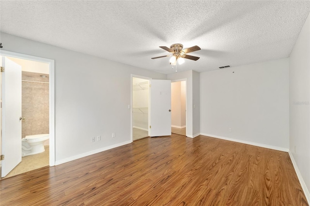 interior space with hardwood / wood-style floors, ceiling fan, a walk in closet, and ensuite bath