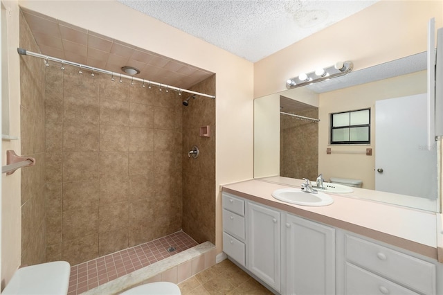 bathroom featuring a tile shower, vanity, a textured ceiling, tile patterned flooring, and toilet