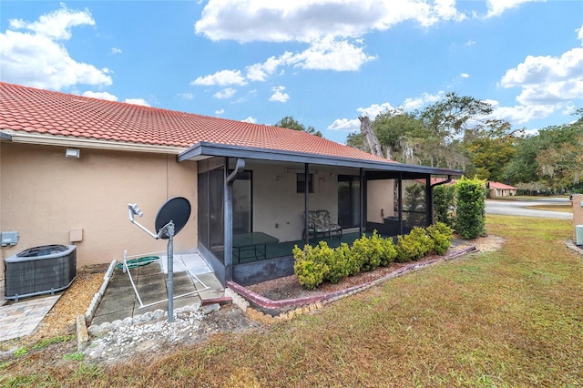 rear view of property with central air condition unit, a sunroom, and a lawn