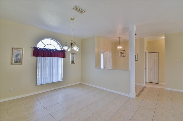 empty room with decorative columns, light tile patterned floors, a textured ceiling, and an inviting chandelier