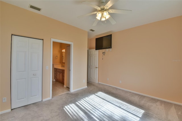 unfurnished bedroom featuring connected bathroom, ceiling fan, a closet, and light colored carpet