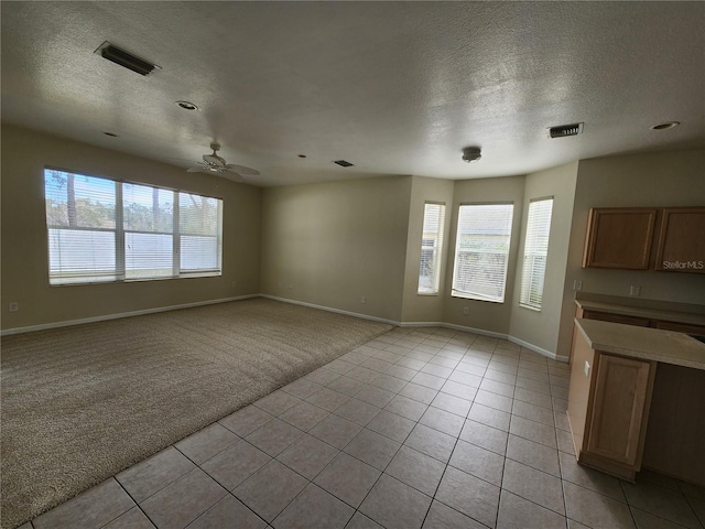 unfurnished living room with a wealth of natural light, ceiling fan, light colored carpet, and a textured ceiling