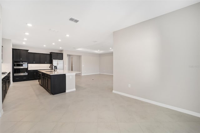 kitchen featuring stainless steel appliances, a tray ceiling, a kitchen island with sink, sink, and light tile patterned flooring