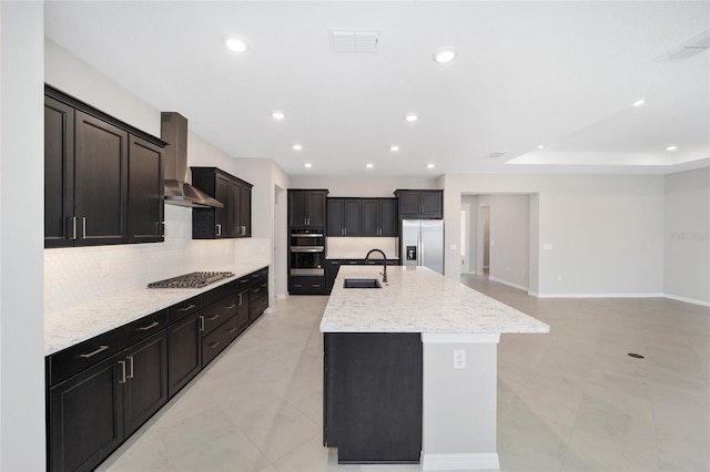 kitchen with decorative backsplash, wall chimney exhaust hood, stainless steel appliances, sink, and an island with sink