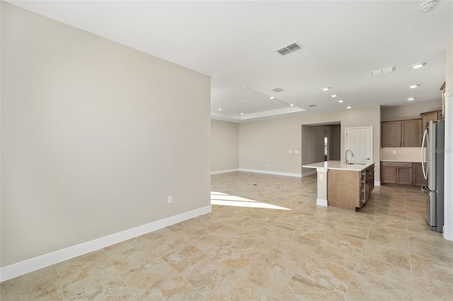 kitchen featuring stainless steel fridge, a kitchen breakfast bar, a raised ceiling, a kitchen island with sink, and sink