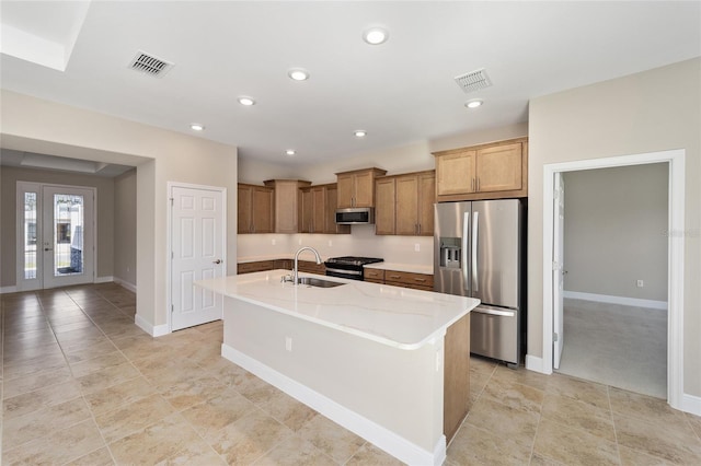 kitchen featuring light stone countertops, sink, an island with sink, light colored carpet, and appliances with stainless steel finishes