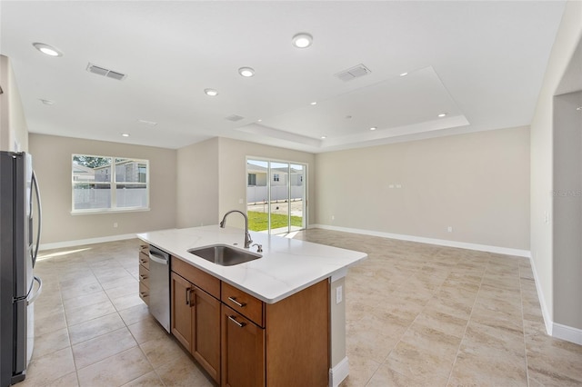 kitchen featuring light stone countertops, sink, stainless steel appliances, a raised ceiling, and a center island with sink