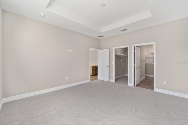 unfurnished bedroom featuring a walk in closet, ensuite bath, a tray ceiling, light colored carpet, and a closet