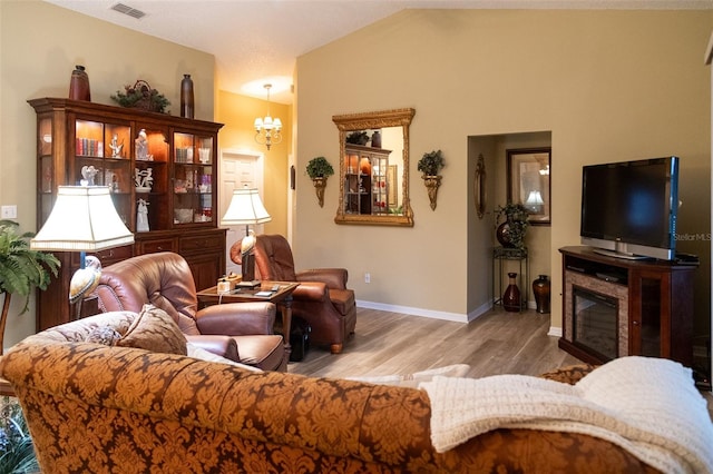 living room with a fireplace, light wood-type flooring, a chandelier, and lofted ceiling