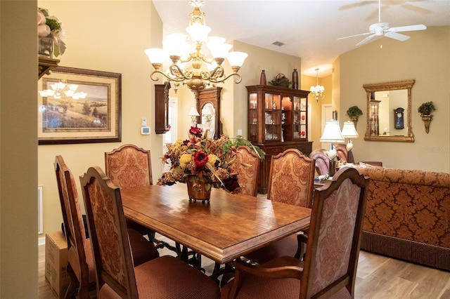 dining room with ceiling fan with notable chandelier, lofted ceiling, and light hardwood / wood-style flooring