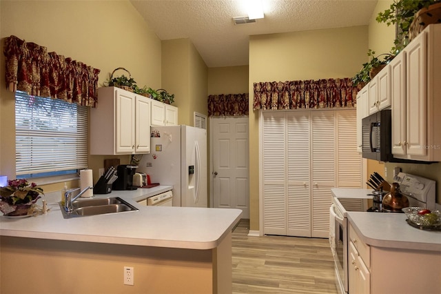 kitchen with kitchen peninsula, light wood-type flooring, a textured ceiling, white appliances, and sink