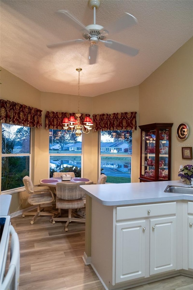 bar with ceiling fan with notable chandelier, a textured ceiling, light hardwood / wood-style flooring, white cabinets, and range