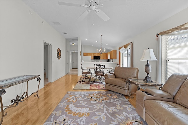 living room featuring ceiling fan with notable chandelier, light wood-type flooring, and vaulted ceiling