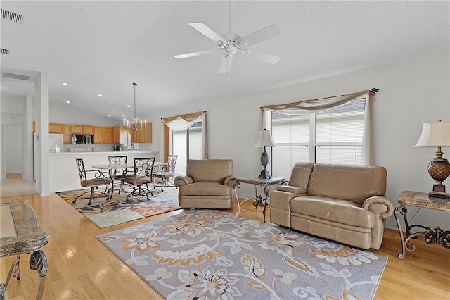 living room with ceiling fan with notable chandelier, light hardwood / wood-style floors, lofted ceiling, and a textured ceiling