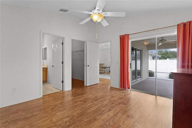 spare room featuring access to outside, vaulted ceiling, a walk in closet, ensuite bathroom, and light wood-type flooring