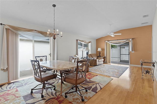 dining area with ceiling fan with notable chandelier, light hardwood / wood-style flooring, vaulted ceiling, and a textured ceiling