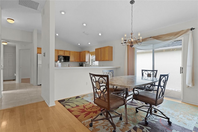 dining area with light wood-type flooring, lofted ceiling, and an inviting chandelier