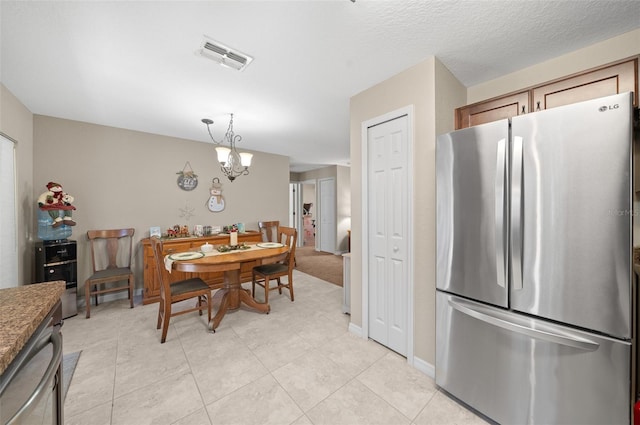 kitchen featuring pendant lighting, an inviting chandelier, stainless steel fridge, light tile patterned floors, and stone countertops