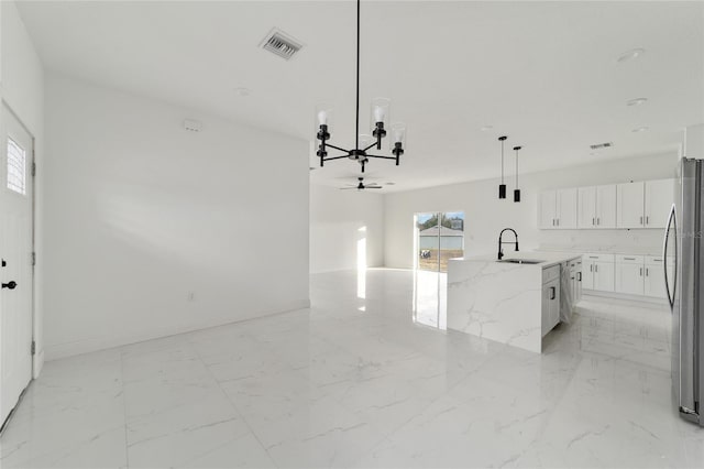 kitchen with light stone countertops, stainless steel appliances, pendant lighting, white cabinetry, and an island with sink