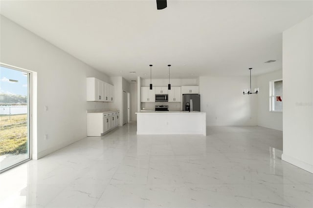 kitchen with white cabinets, decorative light fixtures, stainless steel appliances, and an island with sink