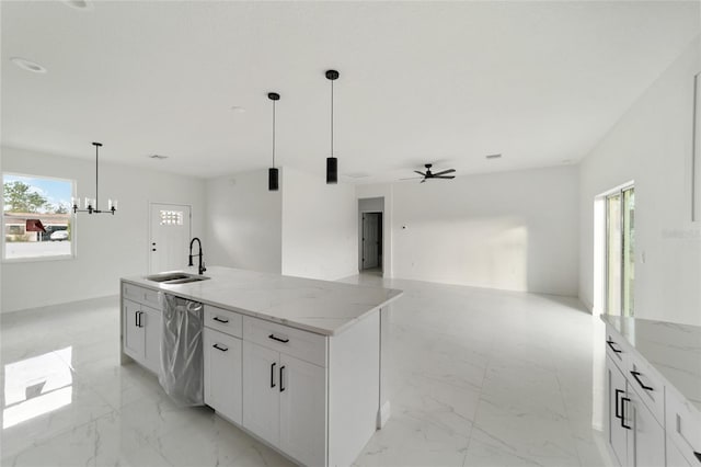 kitchen with a kitchen island with sink, ceiling fan with notable chandelier, sink, stainless steel dishwasher, and white cabinetry