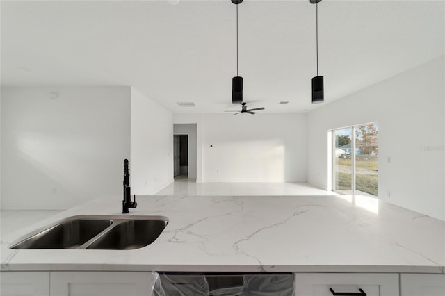 kitchen with light stone counters, sink, white cabinets, and decorative light fixtures