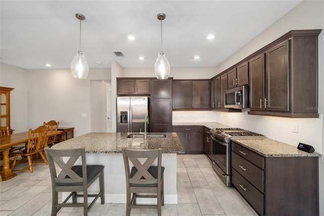 kitchen featuring dark brown cabinetry, stainless steel appliances, sink, decorative light fixtures, and a center island with sink