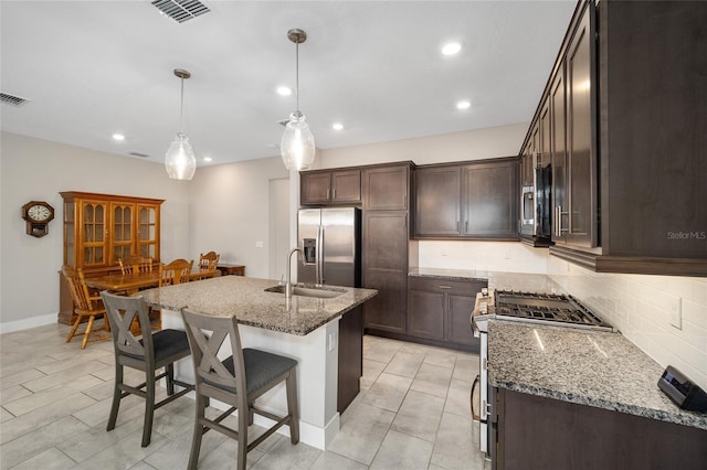 kitchen featuring sink, stone countertops, decorative light fixtures, a center island with sink, and appliances with stainless steel finishes