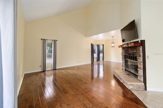 unfurnished living room with hardwood / wood-style flooring, a stone fireplace, and high vaulted ceiling