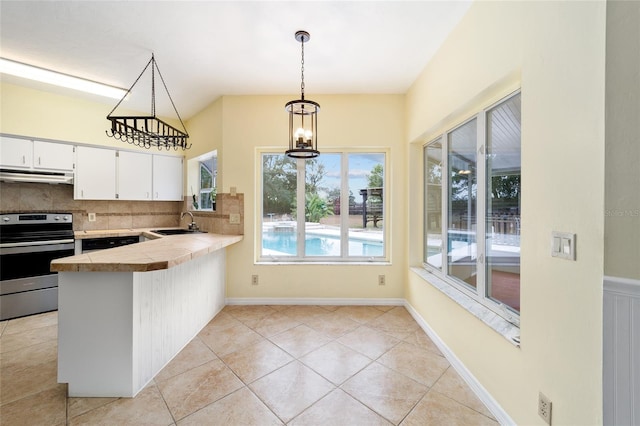 kitchen with kitchen peninsula, tasteful backsplash, exhaust hood, stainless steel stove, and white cabinetry