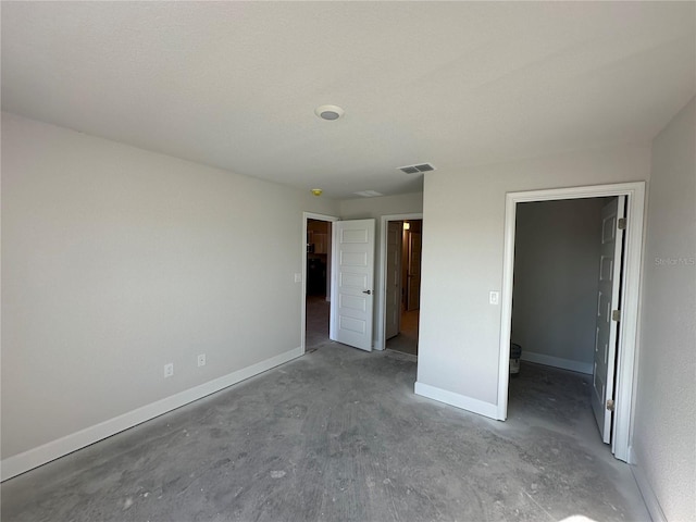 unfurnished bedroom with a textured ceiling, a walk in closet, and concrete floors