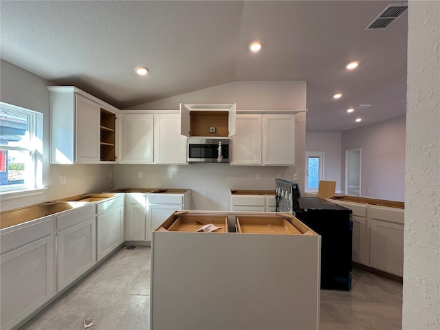 kitchen with white cabinets, a wealth of natural light, a kitchen island, and lofted ceiling