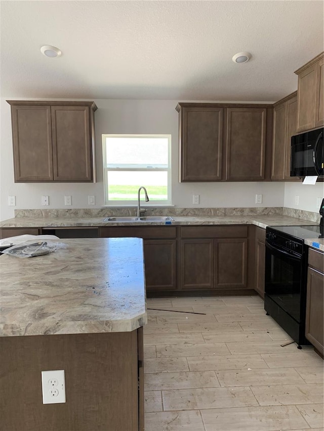 kitchen with dark brown cabinets, sink, light hardwood / wood-style flooring, and black appliances