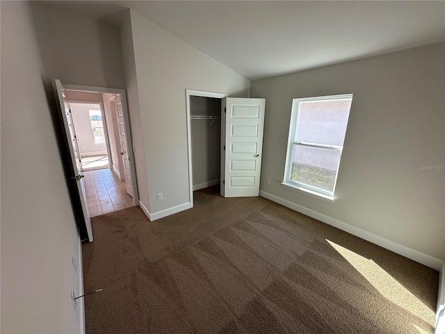 unfurnished bedroom featuring multiple windows, a closet, dark carpet, and lofted ceiling