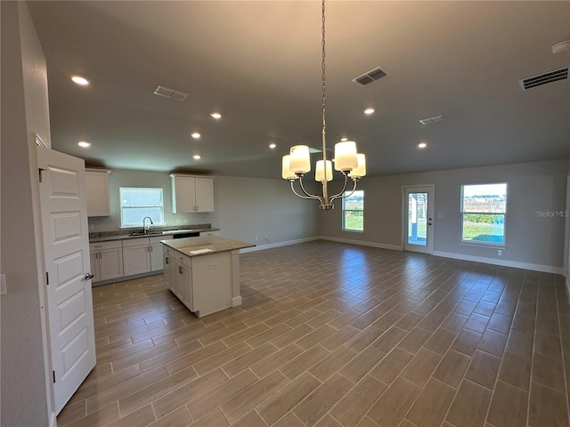 kitchen with decorative light fixtures, a center island, white cabinetry, and light hardwood / wood-style flooring