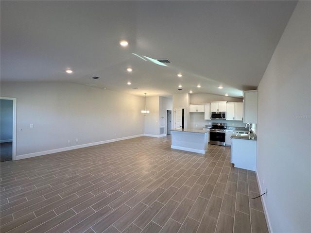 kitchen with appliances with stainless steel finishes, vaulted ceiling, white cabinets, hardwood / wood-style floors, and a center island