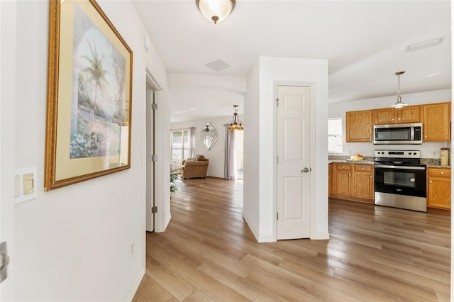 kitchen featuring pendant lighting, light stone counters, light wood-type flooring, and appliances with stainless steel finishes