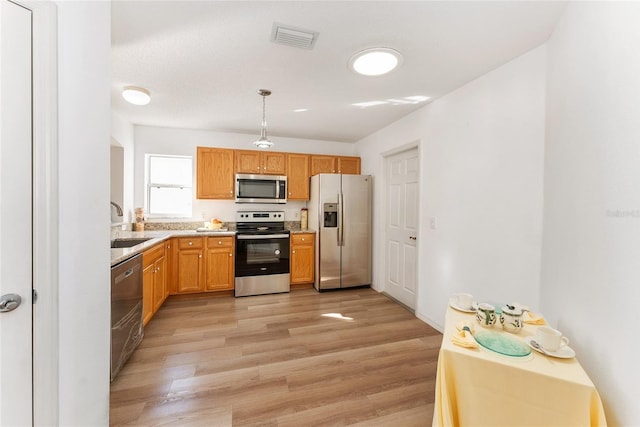 kitchen featuring sink, light hardwood / wood-style floors, decorative light fixtures, and appliances with stainless steel finishes