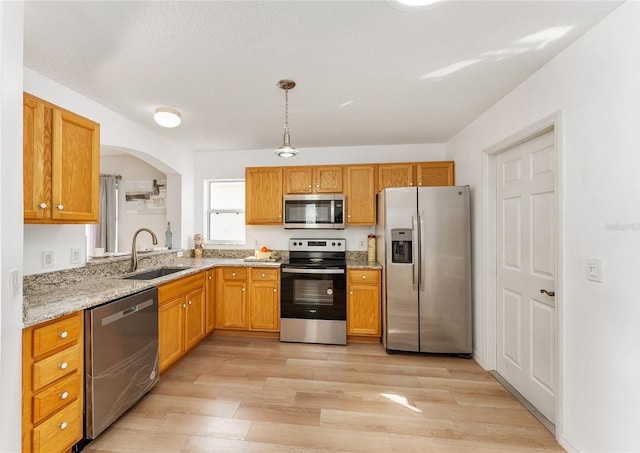 kitchen featuring light stone countertops, appliances with stainless steel finishes, sink, pendant lighting, and light hardwood / wood-style flooring