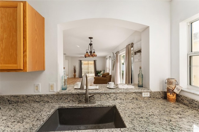 kitchen with light stone counters, sink, and an inviting chandelier