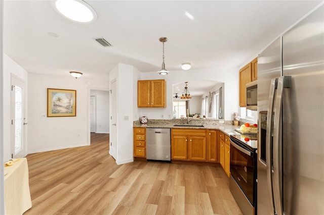 kitchen with light stone countertops, stainless steel appliances, sink, light hardwood / wood-style flooring, and hanging light fixtures