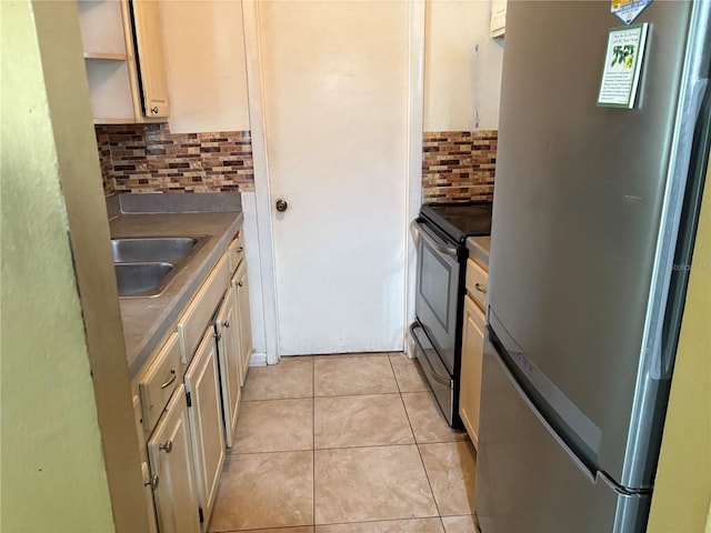 kitchen with light tile patterned floors, sink, cream cabinetry, backsplash, and stainless steel appliances