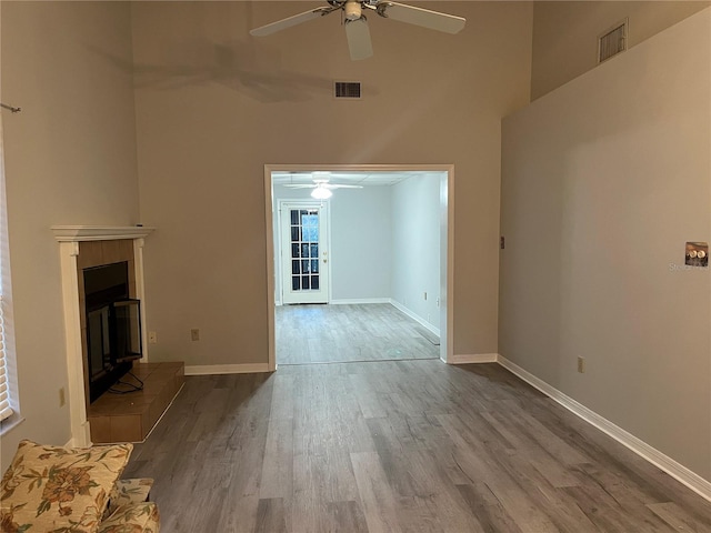 unfurnished living room featuring ceiling fan, a fireplace, a towering ceiling, and light hardwood / wood-style floors