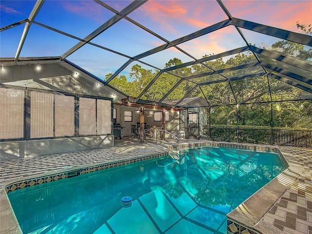 pool at dusk featuring glass enclosure and a patio area