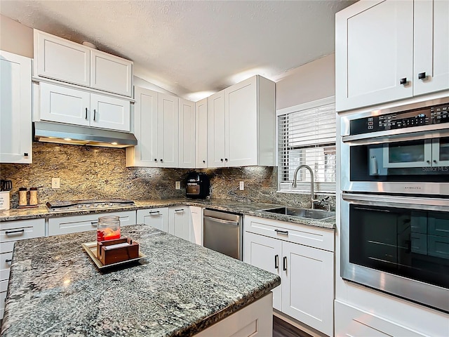 kitchen with stainless steel appliances, white cabinetry, dark stone counters, and sink