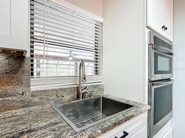 kitchen featuring stainless steel double oven, white cabinetry, sink, and dark stone counters