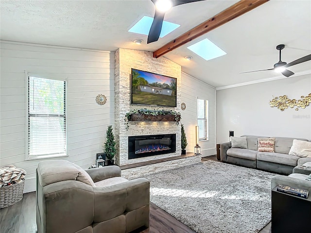 living room featuring dark wood-type flooring, a stone fireplace, wooden walls, ceiling fan, and a textured ceiling