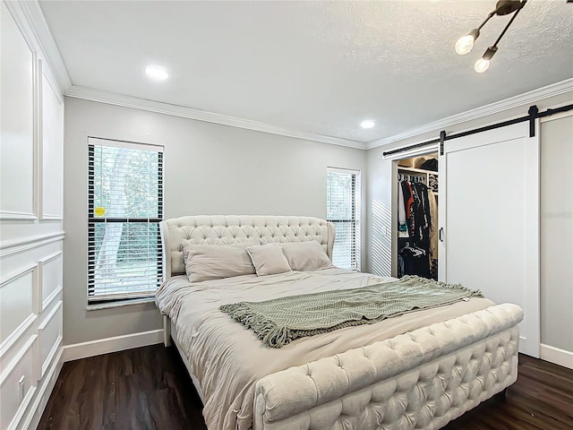 bedroom with a barn door, a walk in closet, dark hardwood / wood-style flooring, and multiple windows