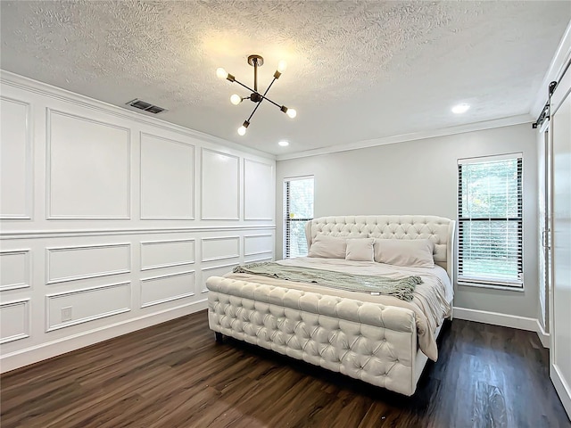 bedroom featuring dark wood-type flooring, a barn door, a notable chandelier, a textured ceiling, and ornamental molding