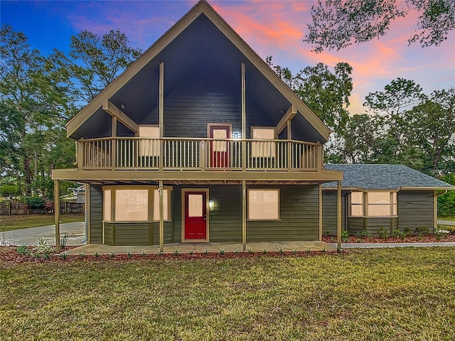 back house at dusk with a wooden deck, a patio area, and a lawn